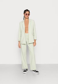 Fato verde menta pálido com um blazer de corte descontraído e calças de perna larga, combinado com um top cropped justo em tom areia e sapatilhas negras.