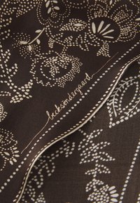 Silk scarf in dark brown with white floral and dot patterns. Features a stitched edge and a signature in an elegant script.