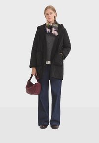Veste matelassée noire avec une capuche en fourrure, portée sur un pull gris, associée à un jean large noir et un sac à main bordeaux.
