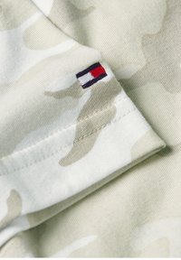 Baumwoll-T-Shirt mit einem hellen Camouflage-Muster in Beige und Weiß. Mit einem kleinen gestickten Logo in Rot, Weiß und Blau am Ärmel.