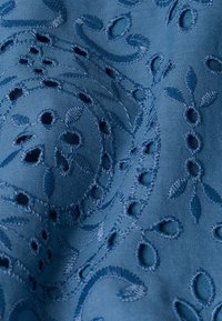 Tela azul bordada con intrincados patrones florales, que presenta diseños cortados y una textura suave, mostrando un tono rico y profundo.
