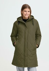 Gequilted parka in donkergroen, voorzien van een capuchon, voorzakken en een midi-lengte snit. Materiaal lijkt zacht en geïsoleerd te zijn.