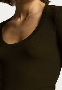 Top ajustado de color verde oliva oscuro con escote en forma de caída, textura acanalada y mangas largas. Detalles de costura a lo largo de los hombros.