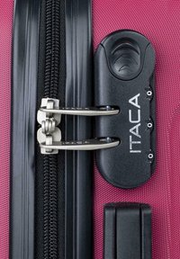 Maleta rosa con un cierre y mecanismo de bloqueo negros, cremalleras de metal plateado y logotipo grabado en el candado. Superficie de tela texturizada.