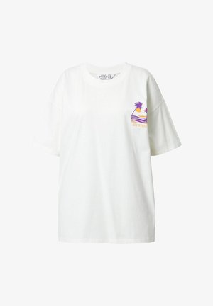 T-shirt en coton blanc à coupe loose, avec un graphisme violet et orange représentant des palmiers et un soleil, portant l'inscription "SEA SEEKER."