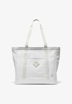 Sac fourre-tout blanc avec longues poignées, poche avant, écusson en forme de losange et petite étiquette de marque rectangulaire en bas à droite.