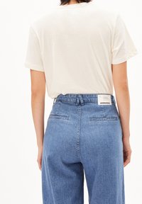 Ljust beige bomull T-shirt med rullade korta ärmar, parat med blå denimbyxor med hög midja och bakfickor.