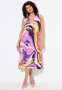 Vestido sin mangas y con escote en V en patrones abstractos multicolores con púrpura, amarillo y negro. Con dobladillo acampanado; combinado con tacones lavanda.