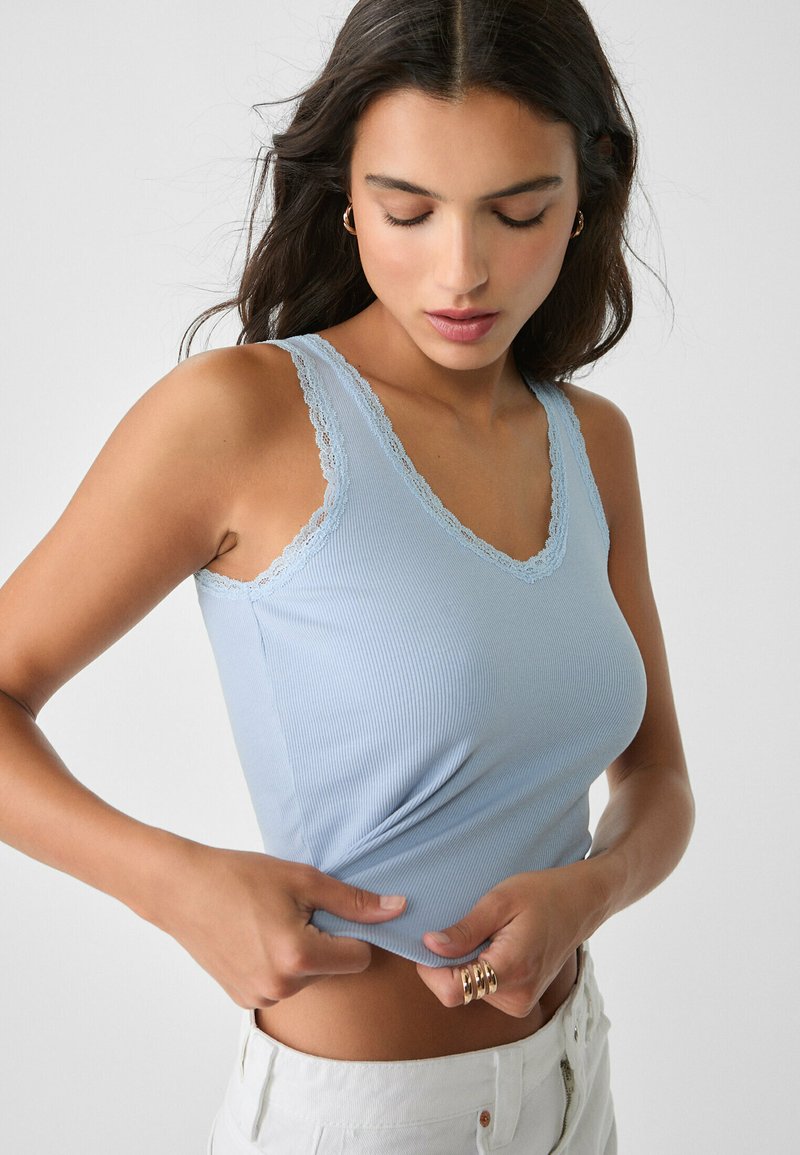 Débardeur côtelé bleu clair avec un col en V et des bordures en dentelle, présentant une coupe ajustée et une texture douce.