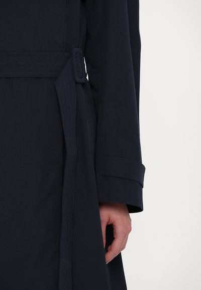 Mornarska trench jakna s pojasom u struku, strukturiranim okovratnikom, detaljima na manžetama i glatkom teksturom. Detaljno šivenje duž pojasa.