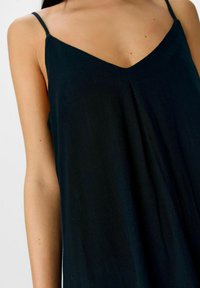 Camisetta nera con design a V, spalline sottili regolabili e una texture di tessuto fluido. Presenta una vestibilità ampia e rilassata.