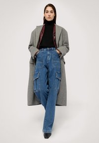 Šedý kabát přes černý rolák, doplněný modrými cargo džíny se bočními kapsami. Černé špičaté podpatky dokončují outfit.