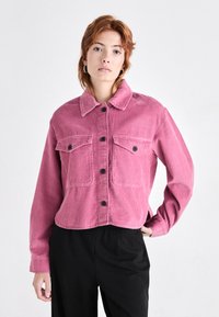 Růžová kordová bunda s cropped designem, předním zapínáním na knoflíky a dvěma náprsními kapsami. Obsahuje límec a dlouhé rukávy.