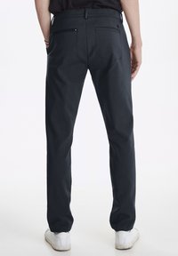 Dark gray trousers with a straight cut, featuring back pockets and a smooth fabric texture. Paired with white sneakers.