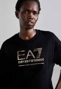Zwarte sweatshirt met een metallic gouden "EA7 Emporio Armani" logo met een gladde textuur. Ronde hals en een ontspannen pasvorm.