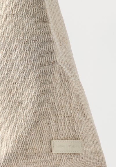 Gros plan sur un sac en tissu beige tissé avec un petit écusson rectangulaire cousu portant un logo.