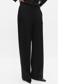 Szerokie czarne spodnie wykonane z gładkiego materiału, z fałdą z przodu i dopasowaną talią. W połączeniu z czółenkami o spiczastych noskach.