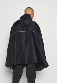 Črn vodoodporen pončo s kapuco, ki ima odsevno belo črto čez hrbet in ohlapen, zračen dizajn.