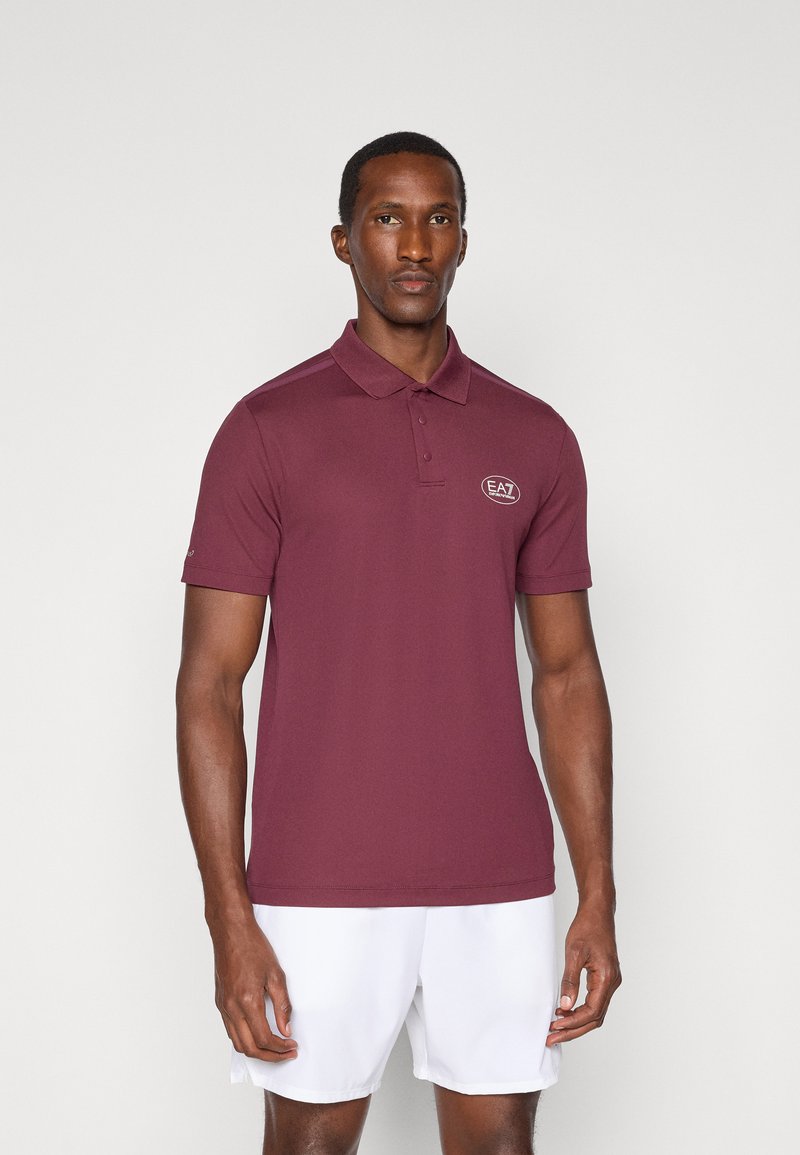 Bordeaux polo majica iz gladkega materiala, s kragnjo na gumbe in majhnim logotipom EA7. Kratki rokavi, ravno dno in prilegajoča zasnova.