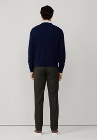 Granatowy sweter z okrągłym dekoltem, zestawiony z ciemnozielonymi spodniami o teksturze i jasnymi butami. Widok od tyłu.