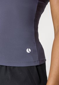 Grå ribbet idretts tank topp med en tettsittende design. Har en hvit logo på siden og en glatt stofftekstur.