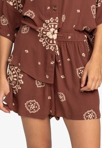 Completo corto con motivo floreale marrone, composto da una camicia con bottoni e pantaloni a shorts con vita elastica, caratterizzato da dettagli color crema e realizzato in un tessuto leggero e morbido.
