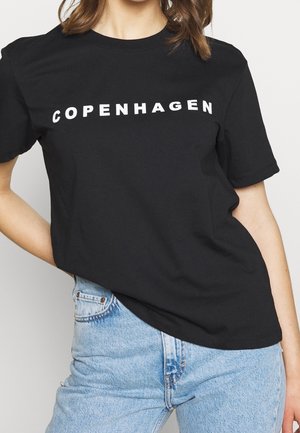 Schwarzes Baumwoll-T-Shirt mit dem Schriftzug "COPENHAGEN" in fetten weißen Buchstaben auf der Vorderseite. Kurze Ärmel und Rundhalsausschnitt. Kombiniert mit hellblauen Jeans.