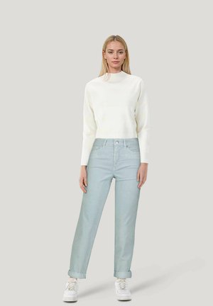 Weißer, kurzgeschnittener Pullover mit langen Ärmeln, kombiniert mit hellblauen, umgeschlagenen Jeans und weißen Sneakern. Einfaches Design und weiche Texturen.