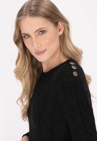 Maglione nero lavorato a maglia con un design testurizzato, caratterizzato da tre bottoni metallici sulla spalla sinistra. Tessuto liscio, vestibilità rilassata.