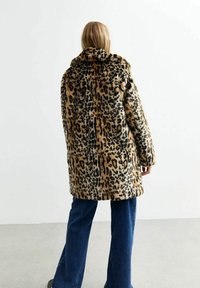 Płaszcz z futra sztucznego w cętkę lamparta z wysokim kołnierzem, długimi rękawami i luźnym krojem, zestawiony z dzwonami niebieskimi dżinsami. W całym wzorze występuje tekstura.