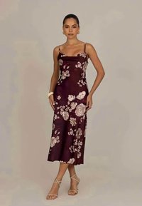 Robe d'été mauve à fleurs avec de fines bretelles, ornée de grandes fleurs de couleur claire ; texture satin lisse ; longueur mi-mollet, associée à des sandales à lanières.