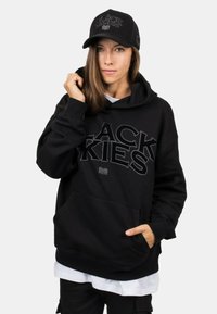 Black hoodie with a front pocket and large embroidered "BLACK SKIES" text. Accompanied by a black cap featuring a logo and mesh back.