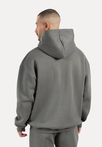 Przewiewny, szary hoodie w oversize'owym fasonie, wykonany z fakturowanej tkaniny, z dużym kapturem, opadającymi ramionami oraz prążkowanymi mankietami i dołem.