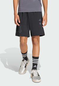 Crne atletske šortsice s elastičnom pojasom, s teksturiranim grafičkim dizajnom. Uparene s crno-bijelim prugastim čarapama i srebrnim cipelama.