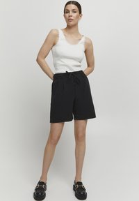 Čierne šortky s elastickým pásom a šnúrkou. Nosené s bielym topom s čipkovým lemom. Čierne loafers s zlatými akcentmi.