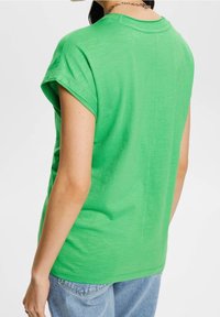 T-shirt verde a maniche corte con vestibilità rilassata e collo a costine, che mostra una texture liscia e un dettaglio del seno posteriore dritto.