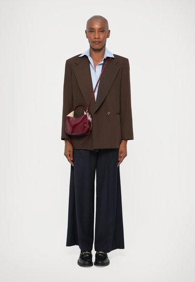Brun oversized blazer over en lyseblå skjorte, parret med brede marineblå bukser. En lille bordeaux håndtaske med en skulderrem. Sorte sko.