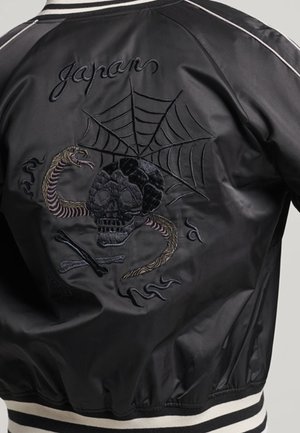 Veste noire avec un crâne brodé, un serpent, une toile d'araignée et des os croisés, avec le mot "Japon" brodé au-dessus.