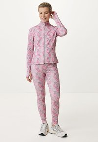 Completo attivo rosa composto da una giacca con zip e leggings aderenti. Il materiale è elasticizzato; il design presenta loghi sovrapposti in rosa chiaro e scuro.