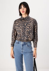 Beige en zwarte luipaardprint knoopshirt met lange mouwen en een ontspannen pasvorm, gecombineerd met lichtblauwe hooggetailleerde jeans.