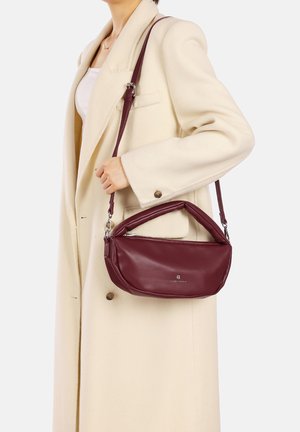 Borsa a mano in pelle bordeaux con forma arrotondata, manico pieghettato e tracolla regolabile; esposta su un cappotto di colore chiaro.