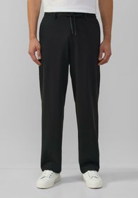 Zwarte, rechte broek met een elastische tailleband en een trekkoord. Gedragen met witte sneakers, met een gladde stoftextuur.