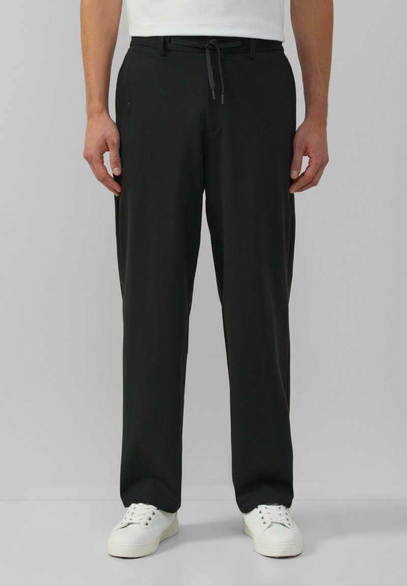 Zwarte, rechte broek met een elastische tailleband en een trekkoord. Gedragen met witte sneakers, met een gladde stoftextuur.