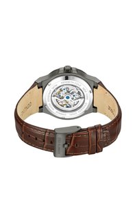 Brūns ādas josta pulkstenis ar nerūsējošā tērauda korpusu, caurspīdīgs aizmugure, kas izceļ mehāniku, apaļa pulksteņa seja un tekstūrēts akcents uz jostas.