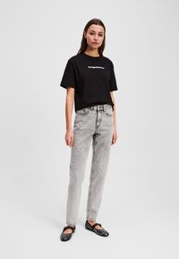T-shirt nera in cotone con testo bianco, abbinata a jeans chiari a vita alta. Ballerine nere con dettagli a borchie bianche. Outfit semplice e casual.