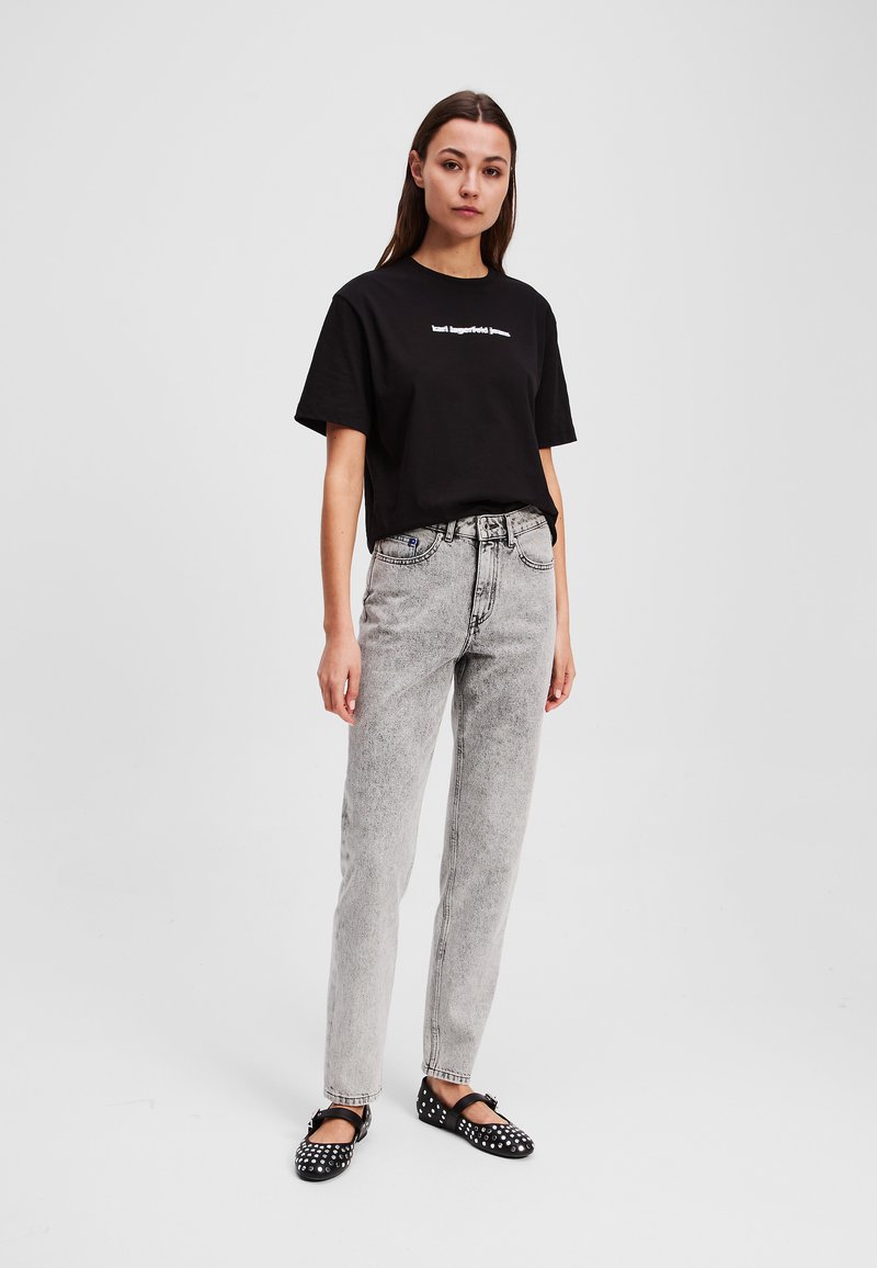 Svart bomullströja med vit text, i kombination med ljusgrå högmidjade jeans. Svarta ballerina-skor med vita nitar. Enkel, avslappnad outfit.