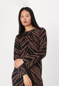 Maglione lavorato a maglia con un motivo a righe zebra marrone e nero, maniche lunghe, scollo rotondo e una silhouette aderente con polsini svasati.