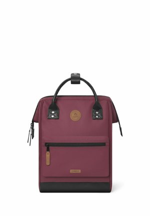 Bordeauxfarbene Rucksack mit schwarzen Akzenten, strukturiertem Boden, Oberhandgriff, vorderer Reißverschlusstasche und rundem Logopatch. Glatte Stoffoberfläche.