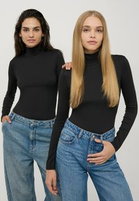 Dwie kobiety noszą dopasowane czarne golfy i jasnobłękitne dżinsy z wysokim stanem. Bluzki mają długie rękawy, a dżinsy charakteryzują się luźnym krojem.