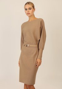 Braunes, geripptes Strickkleid mit Schiffsausschnitt, langen Ärmeln und figurbetonter Silhouette, das ein goldfarbenes Kettenakzent in der Taille hat.